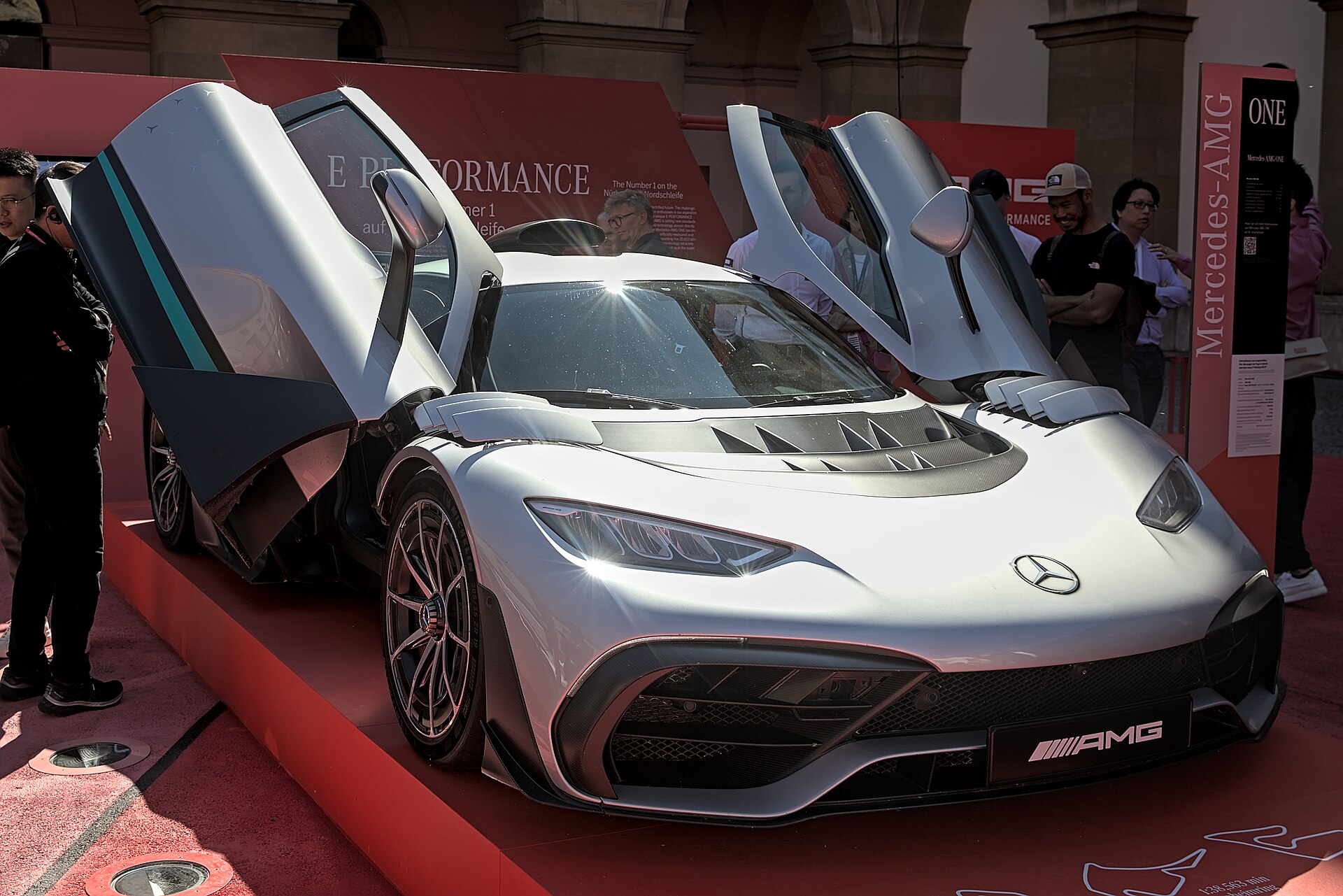 The silver Mercedes-AMG ONE on its show stand, dihedral doors raised, seen from the front three-quarter